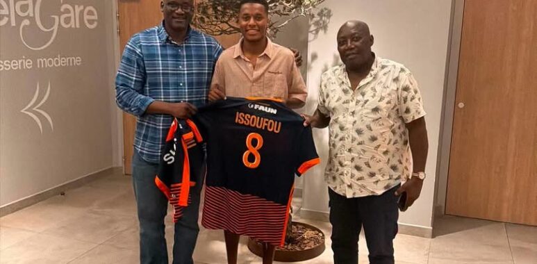 IMG_5847 | AllezPaillade.com Three men pose indoors presenting a black and orange football jersey with name Issoufou and number 8.