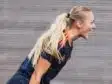 Female soccer player with a blonde ponytail, wearing a navy jersey with orange stripes, leaning forward and shouting.