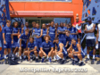 Group of young male athletes in matching blue uniforms posing for a team photo outside a building with orange walls and blue lattice structures; caption reads Montpellier Express 2026.