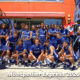 Group of young male athletes in matching blue uniforms posing for a team photo outside a building with orange walls and blue lattice structures; caption reads Montpellier Express 2026.