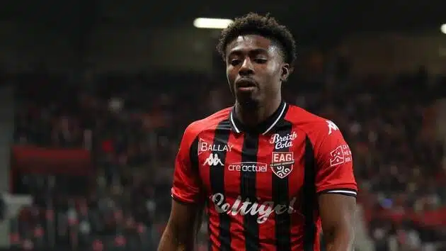 Male soccer player in a red-and-black striped jersey on a green pitch with a blurred crowd in the background.