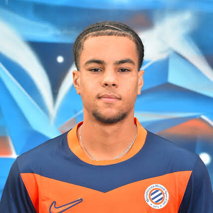 abderrebi-hichem | AllezPaillade.com Portrait of a young man in a blue and orange sports jersey with a circular club badge, standing against a blue graffiti wall.