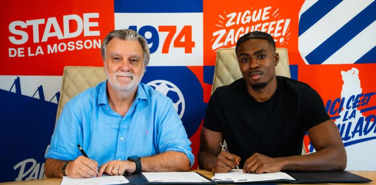 Two men sit at a table signing documents; bright red, blue, and orange mural behind them with 'ALPHA' branding.