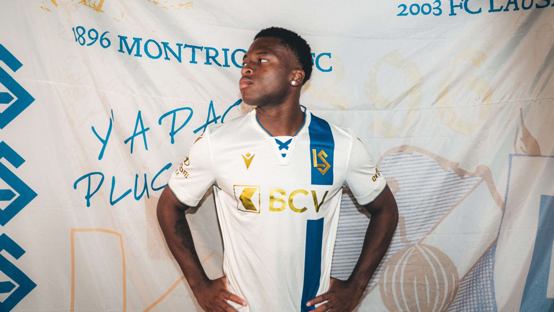 enzo molebe lausanne | AllezPaillade.com Athlete in a white and blue soccer jersey stands with hands on hips in front of a branded backdrop at a sports event.