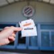 A hand holding a subscription card labeled ABONNEMENT in front of a building entrance with a circular emblem above.
