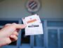 A hand holding a subscription card labeled ABONNEMENT in front of a building entrance with a circular emblem above.