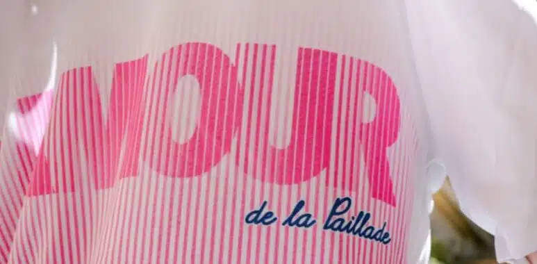 maillot | AllezPaillade.com Close-up of a pink striped logo with large bold letters on white fabric; blue cursive text reads 'de la Paillade'.