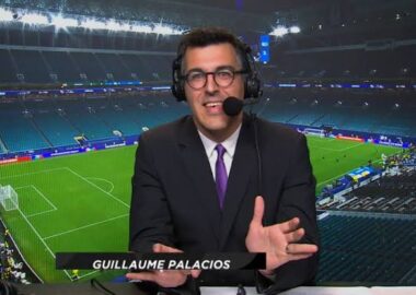 palacios | AllezPaillade.com Sports commentator in a suit and headset speaks into a microphone in a stadium, name visible as Guillaume Palacios.