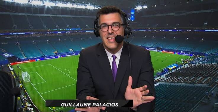 Sports commentator in a suit and headset speaks into a microphone in a stadium, name visible as Guillaume Palacios.