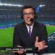 Sports commentator in a suit and headset speaks into a microphone in a stadium, name visible as Guillaume Palacios.