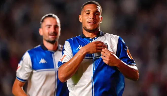 6a9fbbfbe6495 | AllezPaillade.com Two soccer players in blue-and-white kits celebrate on the field, the forward adjusting his jersey as a teammate smiles behind him.