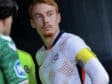 Soccer player in a white jersey with a yellow captain's armband on the left arm, standing with a focused expression.