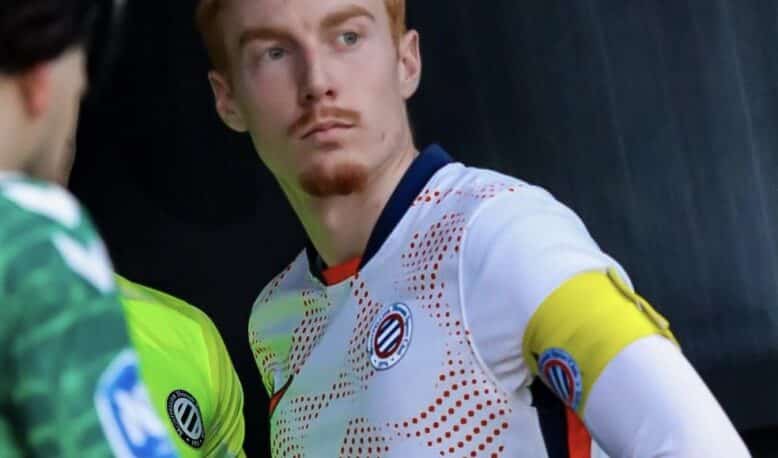 Soccer player in a white jersey with a yellow captain's armband on the left arm, standing with a focused expression.