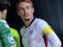 Soccer player in a white jersey with a yellow captain's armband on the left arm, standing with a focused expression.