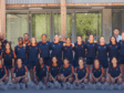Diverse group of athletes in navy and orange uniforms posing for a team photo outside a building.