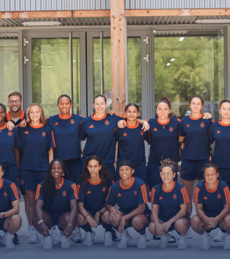 Diverse group of athletes in navy and orange uniforms posing for a team photo outside a building.