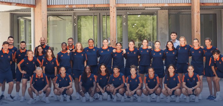 Diverse group of athletes in navy and orange uniforms posing for a team photo outside a building.