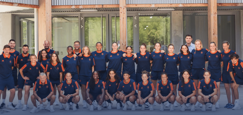 Diverse group of athletes in navy and orange uniforms posing for a team photo outside a building.