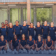 Diverse group of athletes in navy and orange uniforms posing for a team photo outside a building.