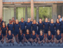 Diverse group of athletes in navy and orange uniforms posing for a team photo outside a building.