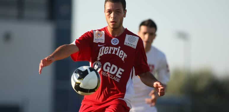 Soccer player in a red kit controls a black-and-white ball during a match, with another player in white in the background.