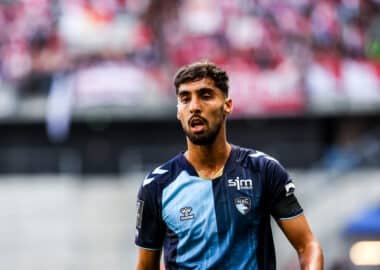 Soccer player in a blue jersey on the field with a blurred crowd in the stands behind him