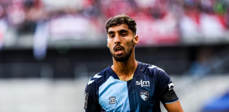 Soccer player in a blue jersey on the field with a blurred crowd in the stands behind him