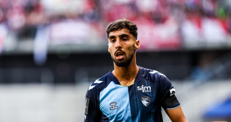 Soccer player in a blue jersey on the field with a blurred crowd in the stands behind him