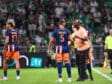 Soccer players in blue&ndash;orange uniforms on a green pitch sharing a moment as a referee speaks nearby, crowded stands in the background.
