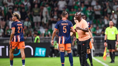 Soccer players in blue&ndash;orange uniforms on a green pitch sharing a moment as a referee speaks nearby, crowded stands in the background.