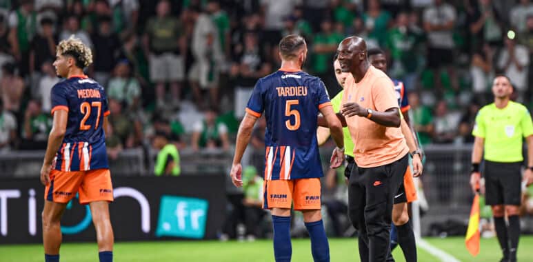 Soccer players in blue&ndash;orange uniforms on a green pitch sharing a moment as a referee speaks nearby, crowded stands in the background.