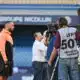 Athlete in a peach hoodie being interviewed by a TV crew with cameras at a stadium backdrop.