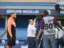 Athlete in a peach hoodie being interviewed by a TV crew with cameras at a stadium backdrop.