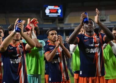 Soccer players in blue and orange striped uniforms celebrate, raising blue water bottles on the field.