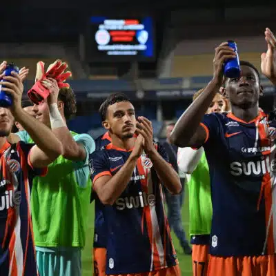 Soccer players in blue and orange striped uniforms celebrate, raising blue water bottles on the field.