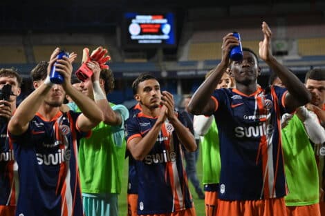 Soccer players in blue and orange striped uniforms celebrate, raising blue water bottles on the field.