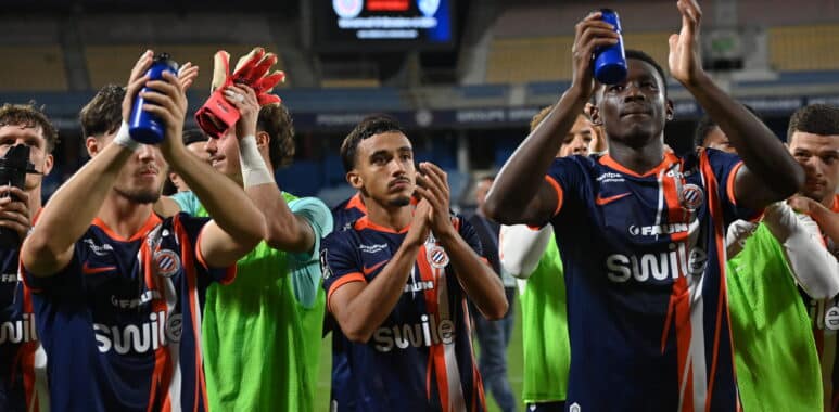 Soccer players in blue and orange striped uniforms celebrate, raising blue water bottles on the field.