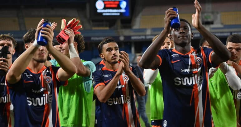 Soccer players in blue and orange striped uniforms celebrate, raising blue water bottles on the field.