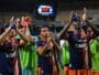 Soccer players in blue and orange striped uniforms celebrate, raising blue water bottles on the field.