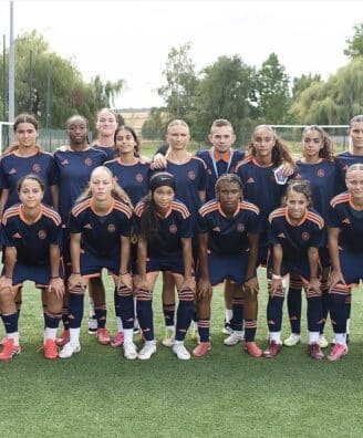 Girls' soccer team posing for a group photo on a green field in navy blue and orange uniforms.