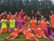 Youth soccer team posing with fists up after a game on a grassy field, orange uniforms with a few in neon vests.