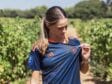 Woman in a navy blue sports jersey with orange accents stands in a vineyard, looking down as she adjusts her shirt.