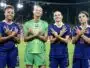 Four female French soccer players stand on a stadium pitch, smiling and crossing their arms over their chests in a show of unity.
