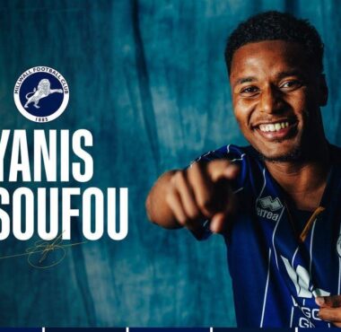 Promotional banner: smiling player in blue pinstripe jersey pointing at the camera with Millwall crest and the text 'YANIS ISSOUFOU' on a teal backdrop; 'WELCOME TO MILLWALL' unreadable at top-right.