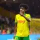Soccer player in yellow and green kit on the field, pointing with his right hand during a match.