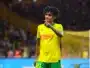 Soccer player in yellow and green kit on the field, pointing with his right hand during a match.